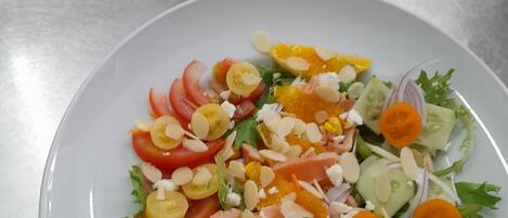 Two plates of salad with various ingredients like tomatoes, cucumbers, and cheese on a stainless steel table.
