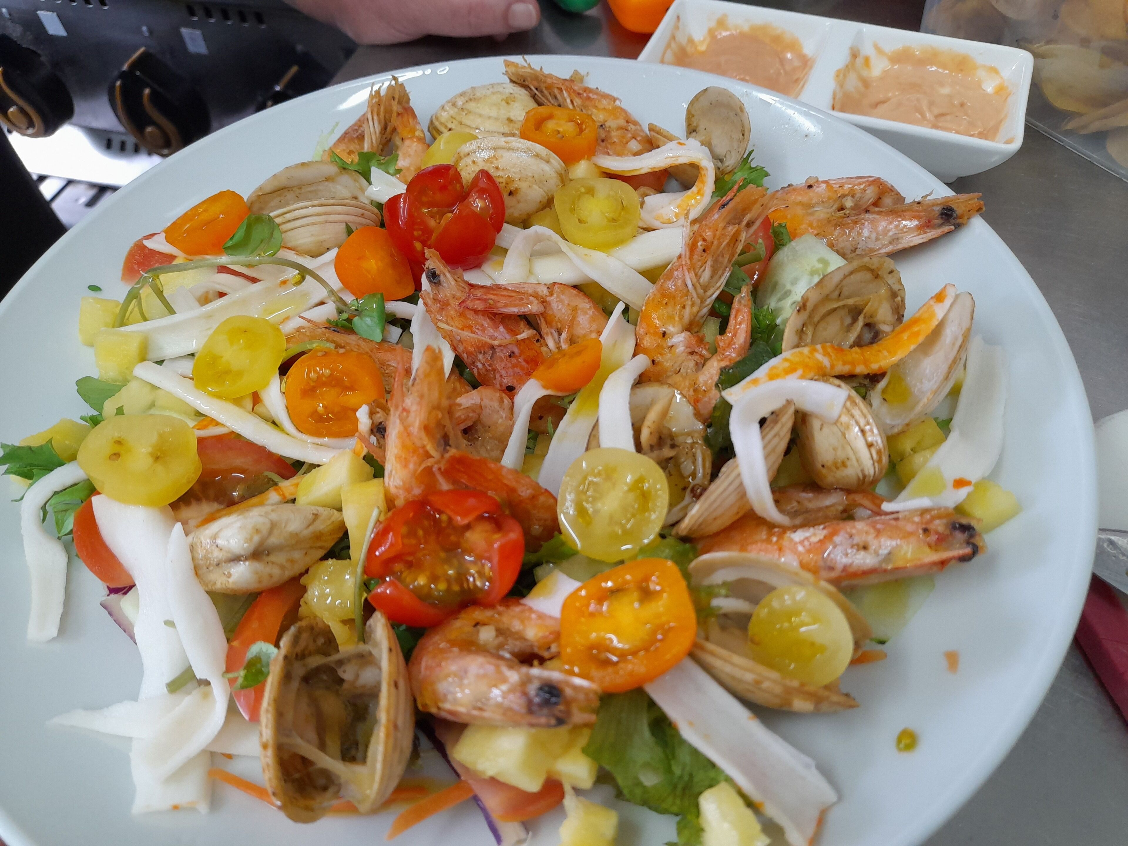 A seafood salad with shrimp, clams, and vegetables on a white plate.