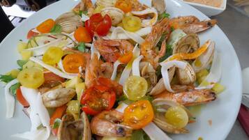 Une salade de fruits de mer composée de crevettes, de palourdes et de légumes, servie dans une assiette blanche.