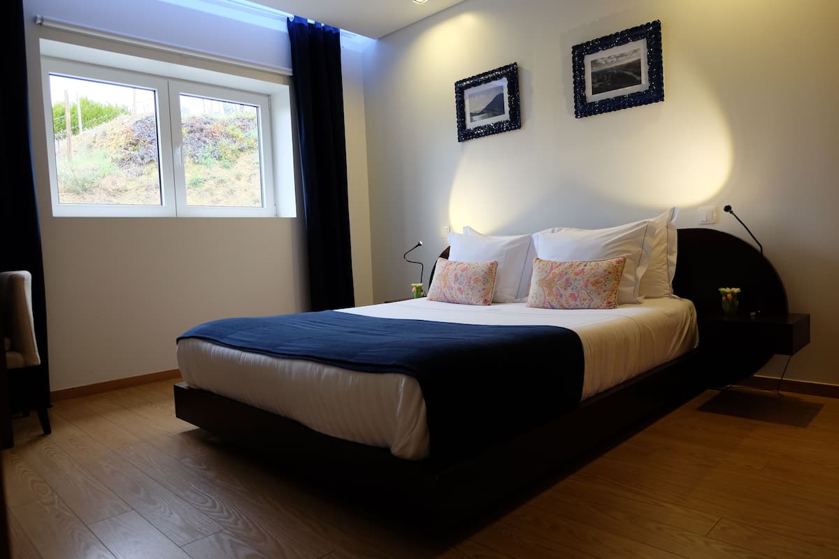 A bedroom with a bed, a nightstand, a lamp, a window with curtains, and two framed pictures on the wall.