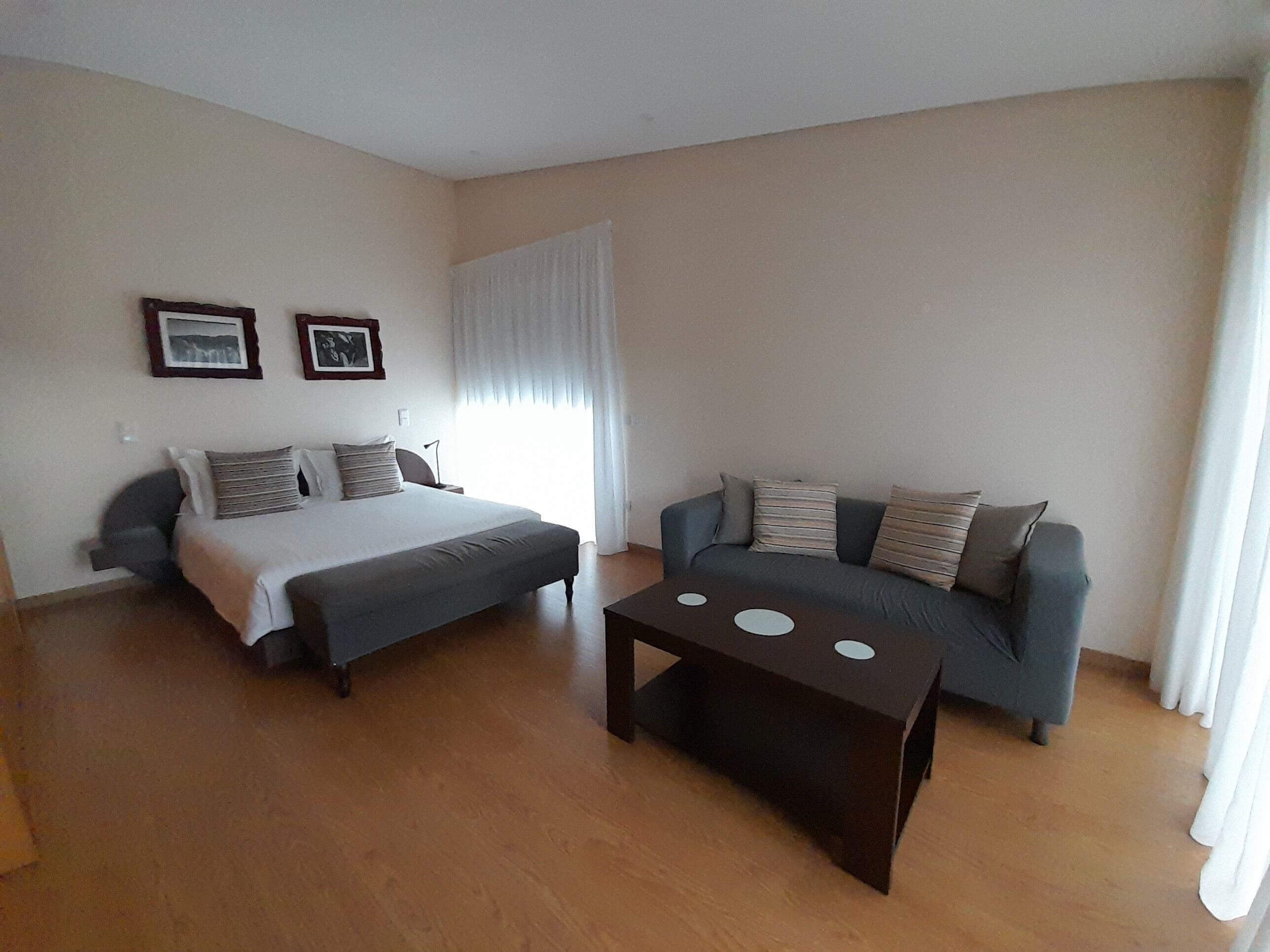 A bedroom with a bed, a sofa, and a coffee table. There are two framed pictures on the wall.