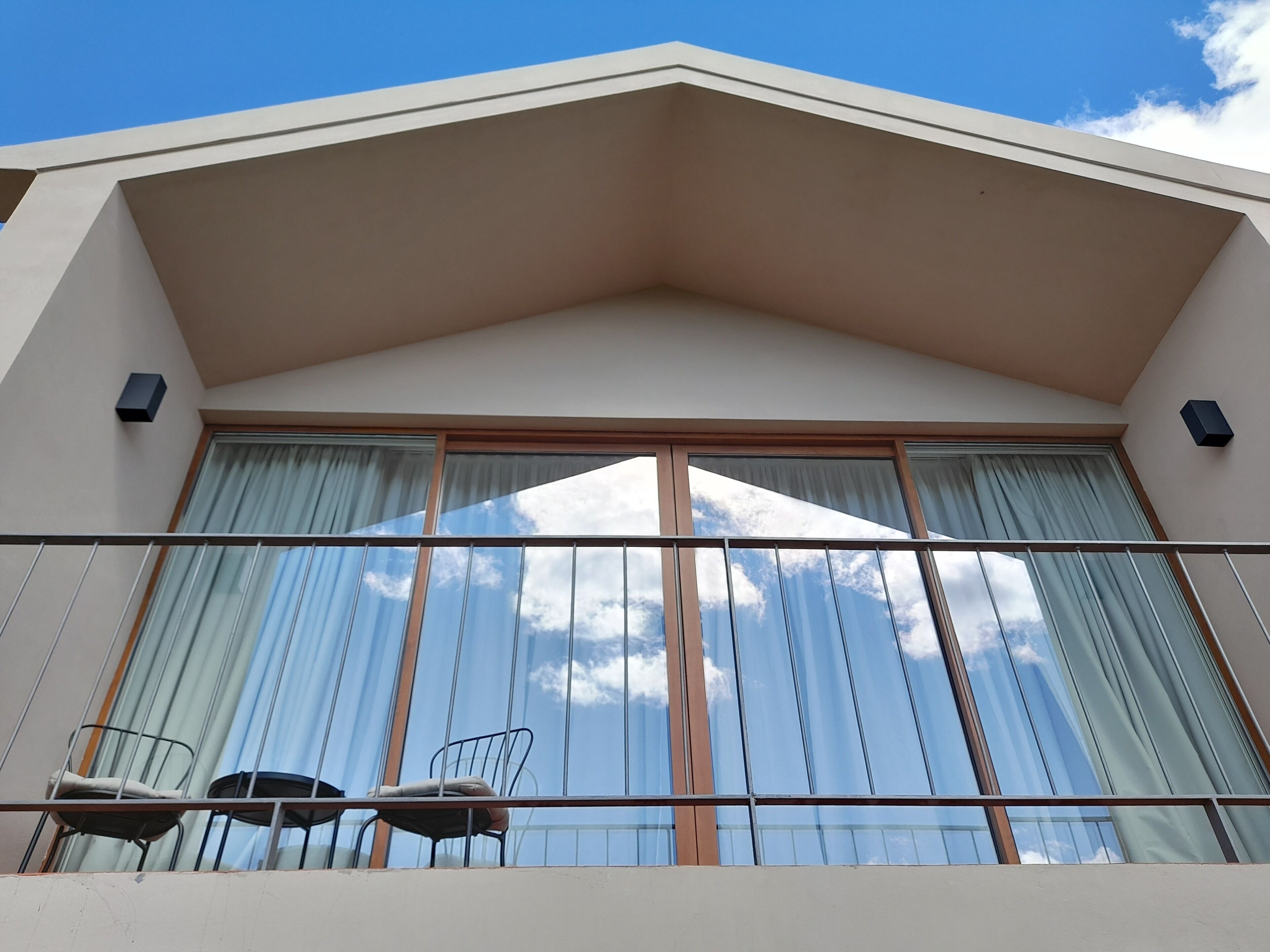 A balcony with a view of the sky, a railing, and two chairs.