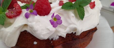 Un gâteau garni de crème fouettée et de framboises, présenté sur une assiette blanche.