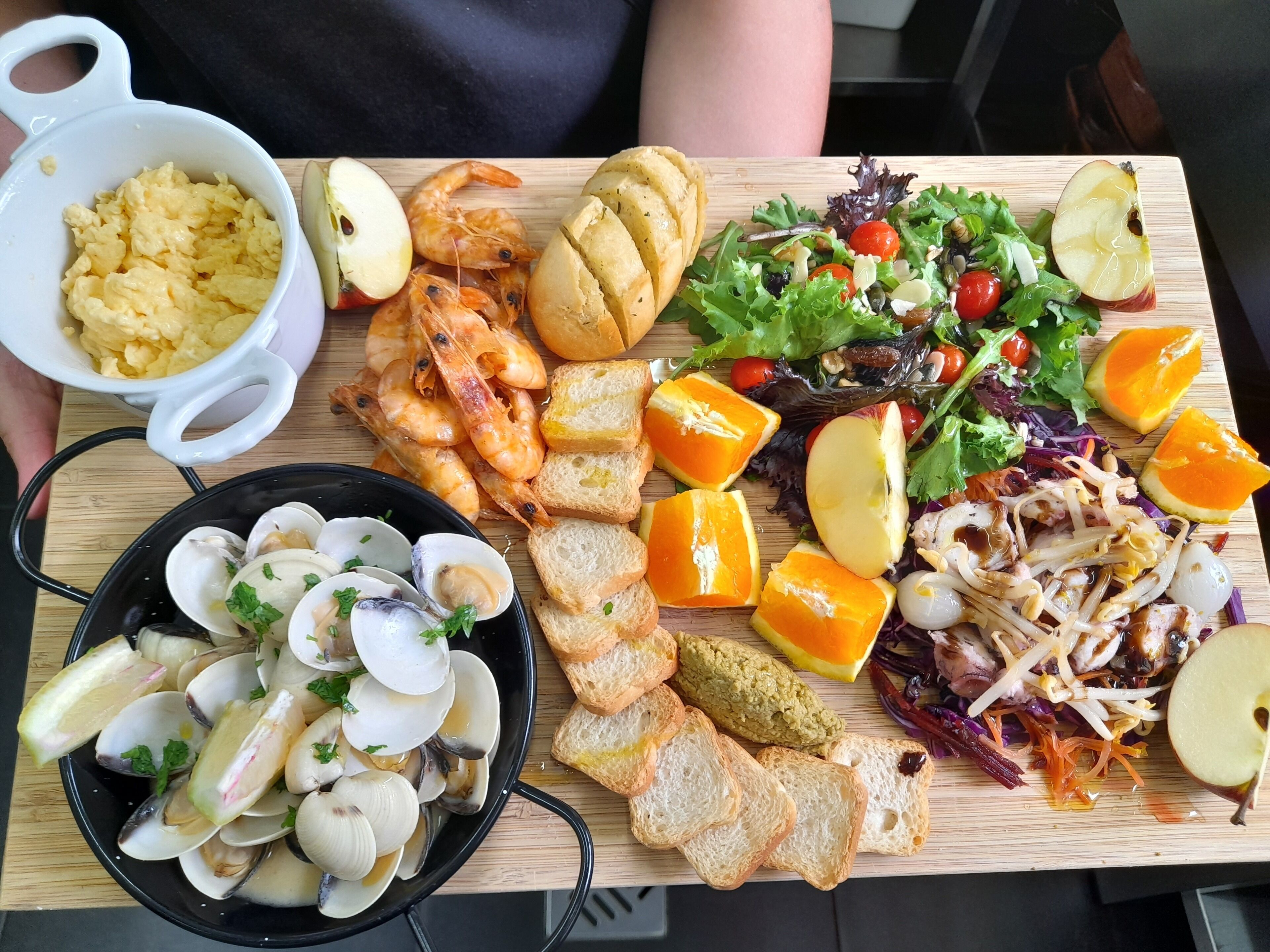 Una tabla de madera con diversos alimentos, como camarones, almejas, pan y una ensalada.