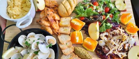 Una tabla de madera con diversos alimentos, como camarones, almejas, pan y una ensalada.