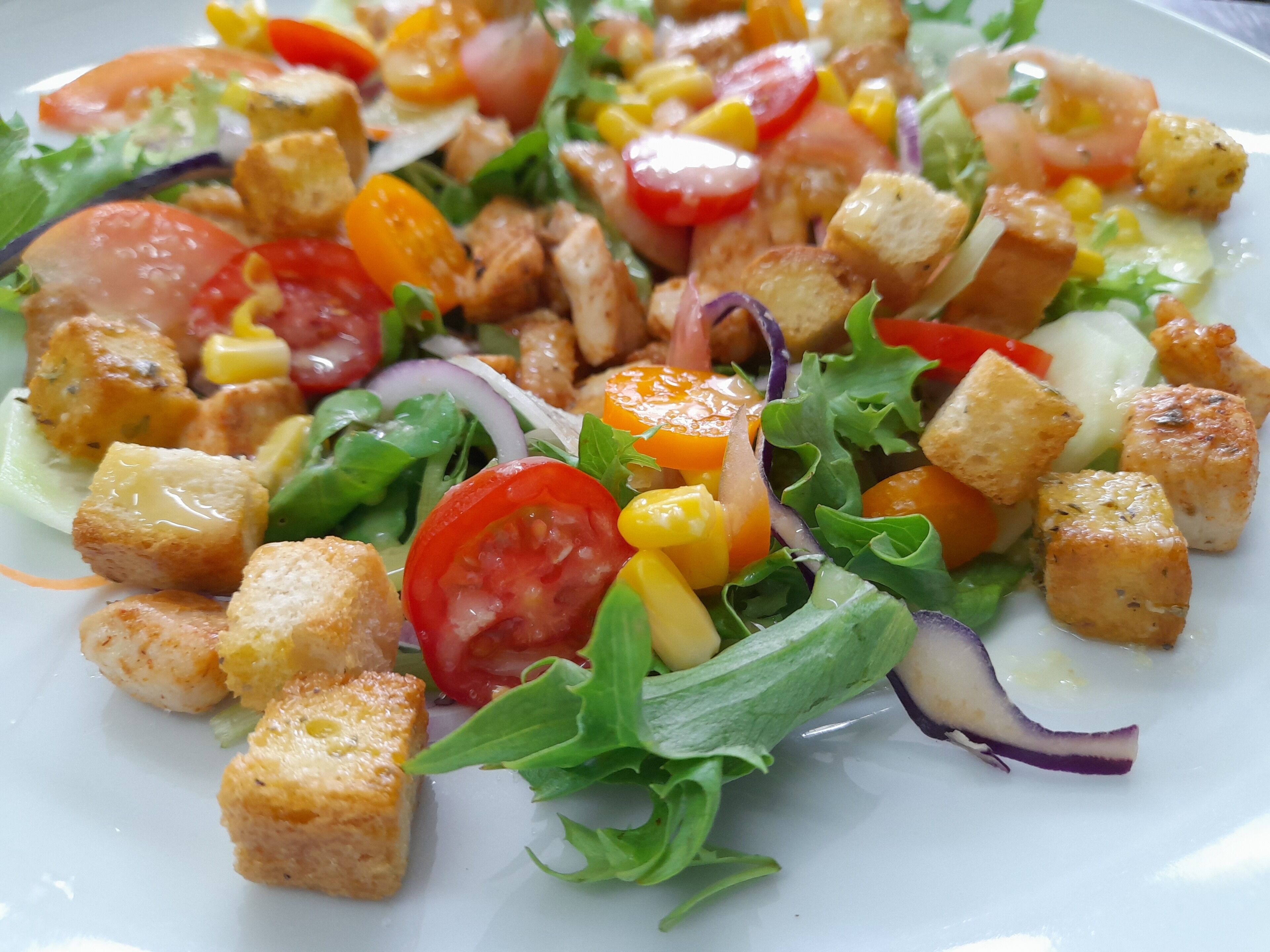 Ensalada con diferentes verduras y croutons sobre un plato blanco.