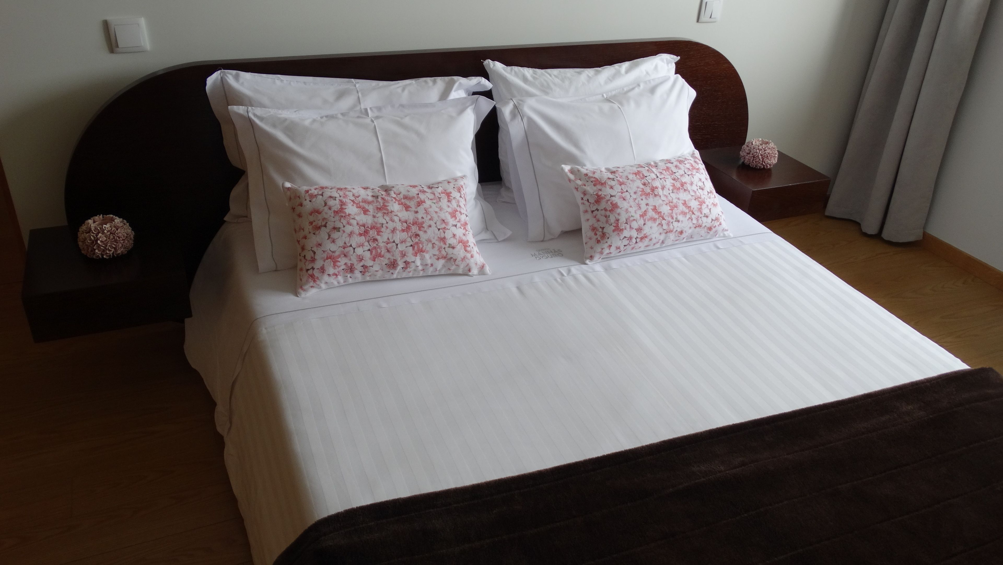 A neatly made bed with white and floral pillows, a dark headboard, and a wooden nightstand with a decorative item.