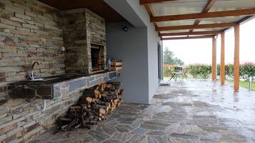 Una chimenea de piedra con un lavamanos, leña apilada y un patio cubierto con vistas a un jardín.