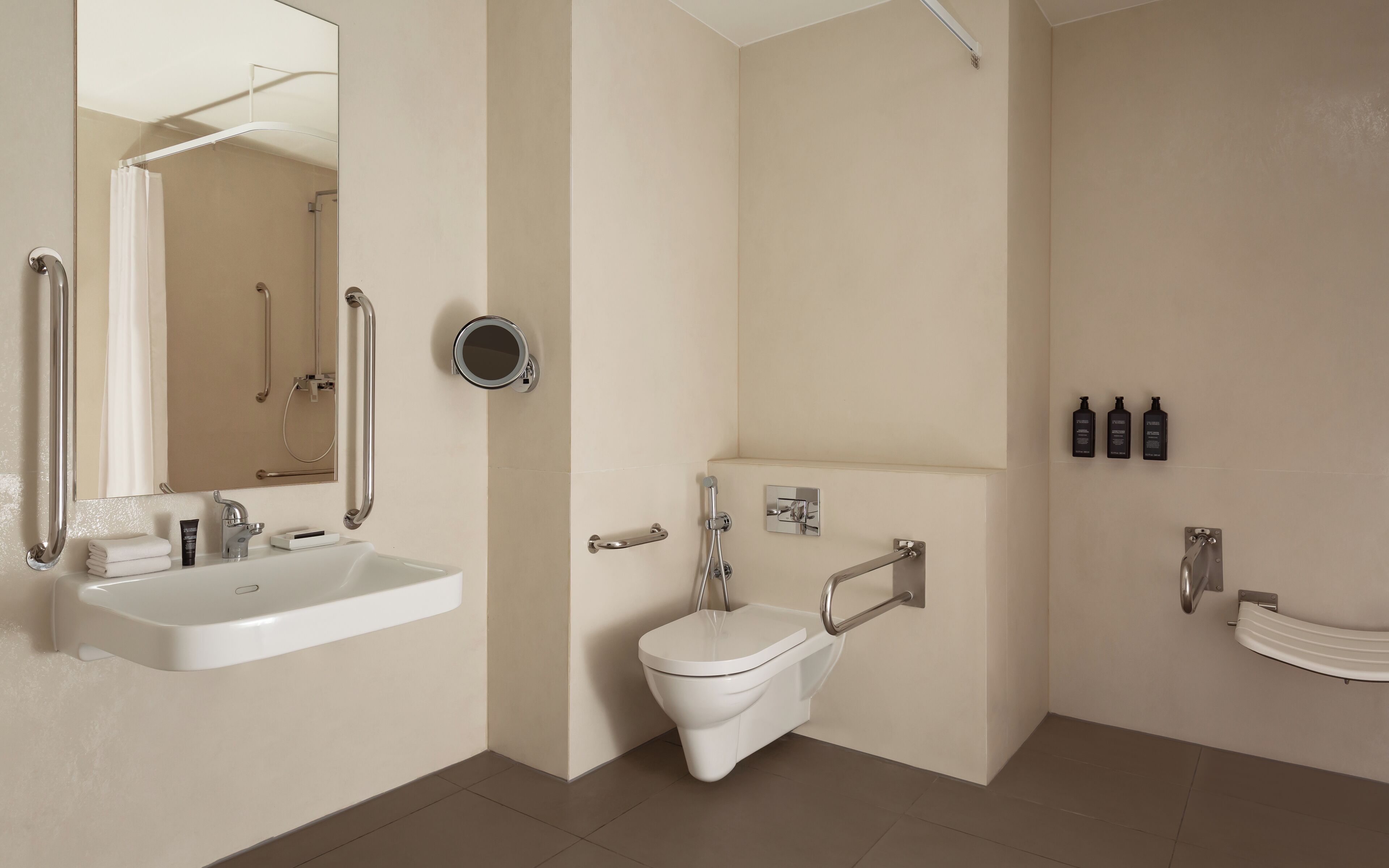 Et moderne badeværelse med håndvask, toilet og brusebad. Der er gelændere og et spejl.