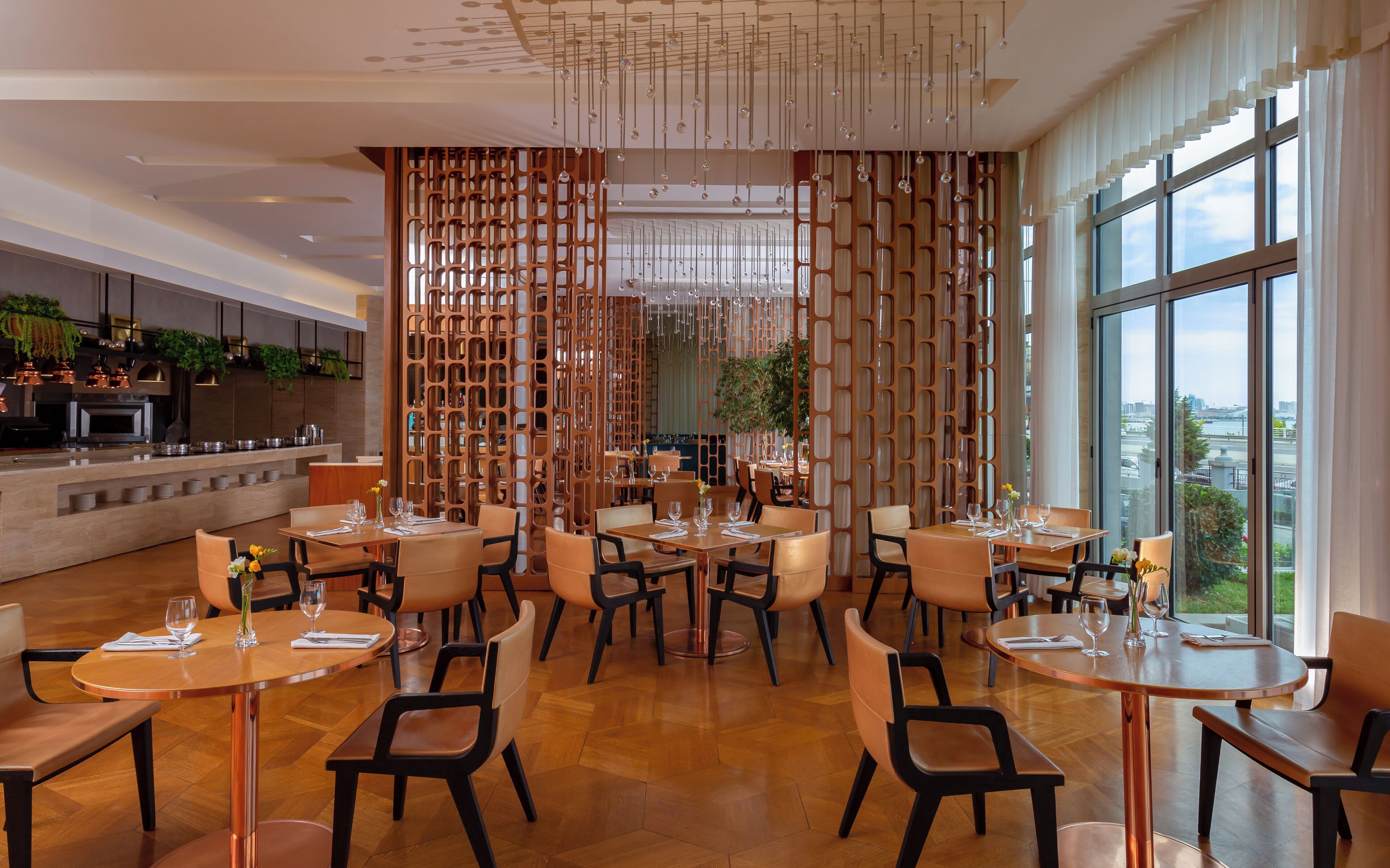 A modern restaurant with wooden furniture, a central decorative screen, and large windows offering a city view.