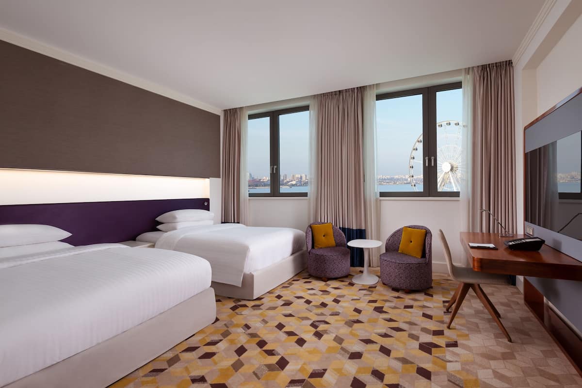 A hotel room with two beds, a desk, a chair, and a view of a Ferris wheel.