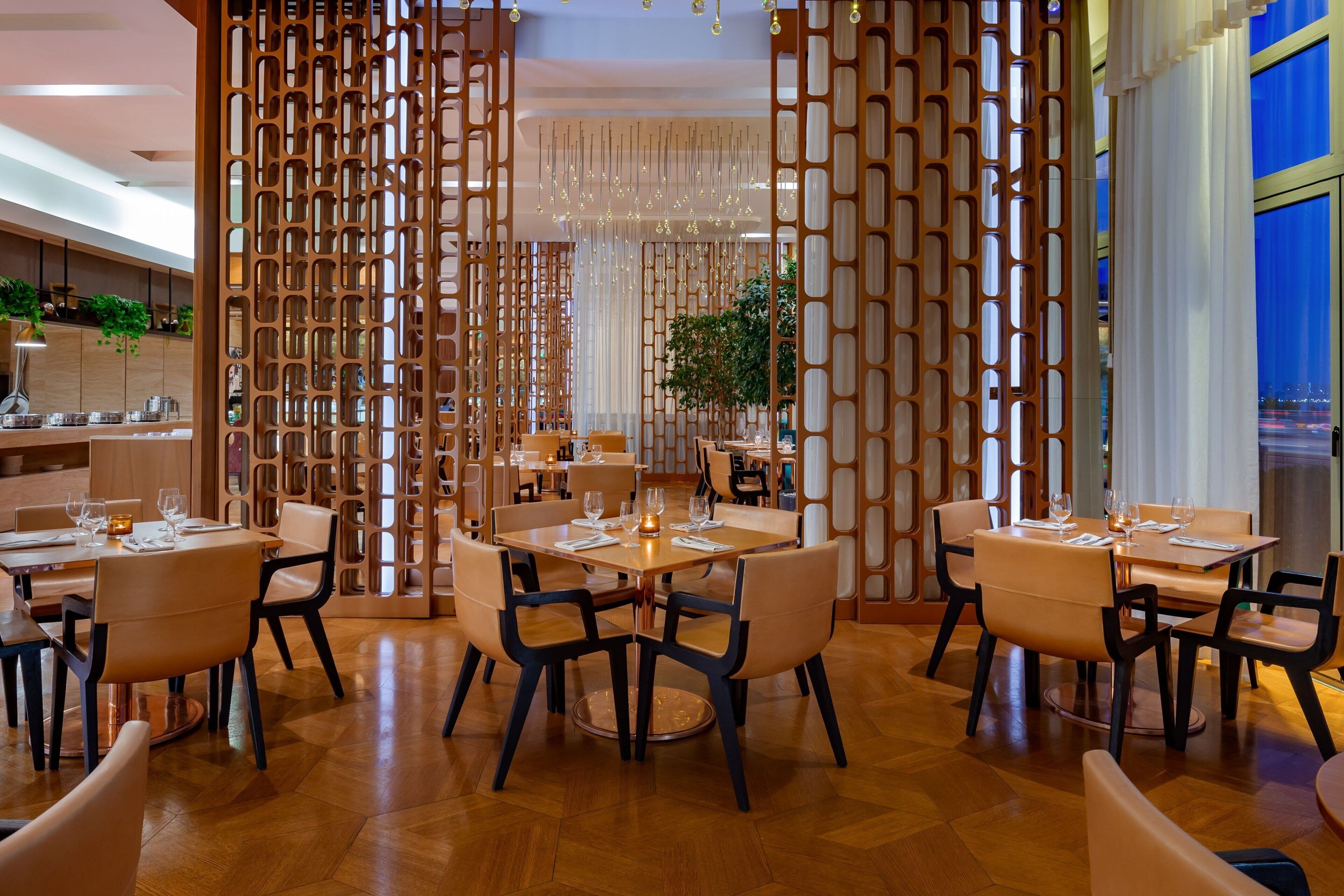 A modern restaurant with wooden partitions, round tables, and comfortable seating.