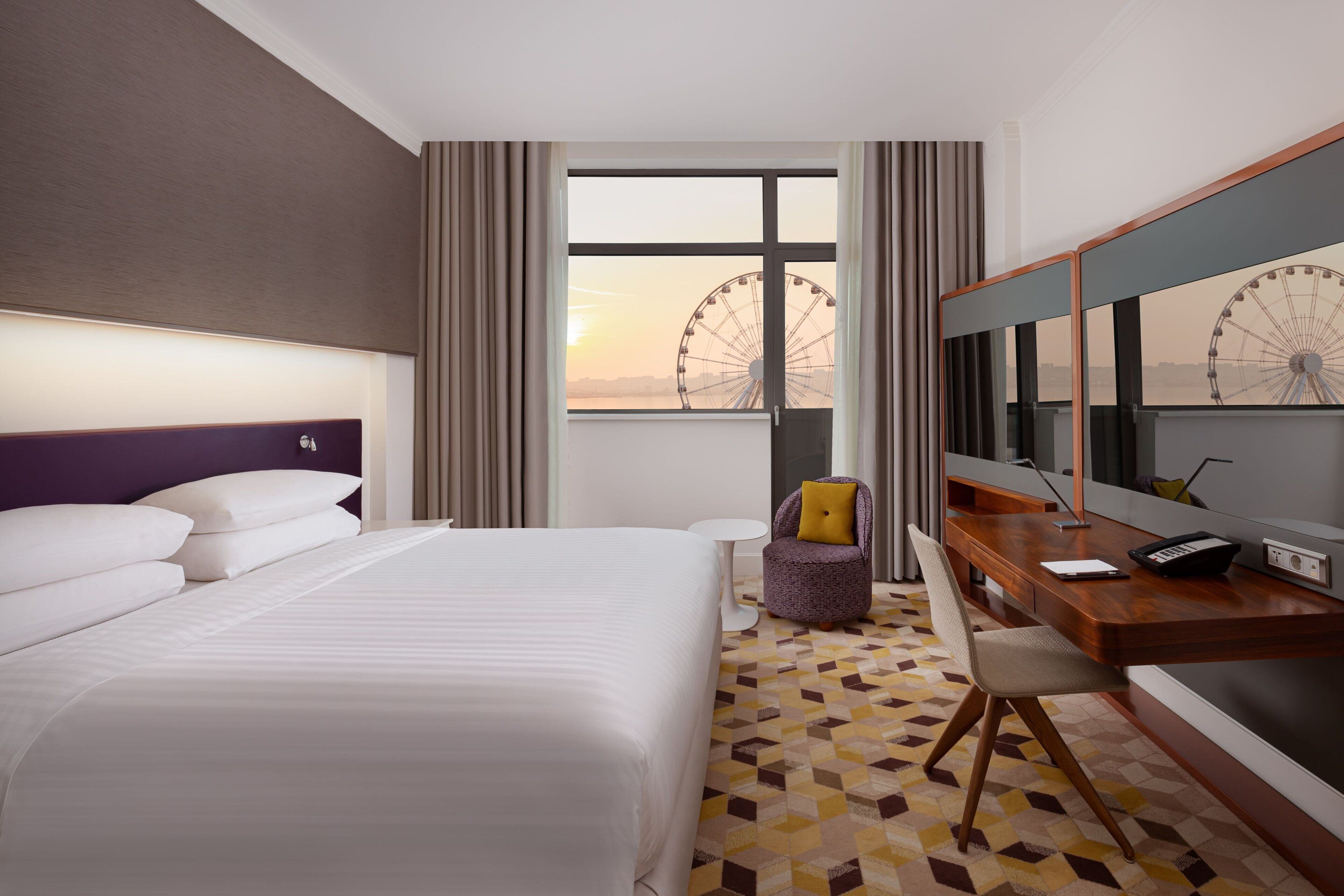 Hotelkamer met een groot bed, een bureau met stoel, een klein rond tafeltje en uitzicht op een reuzenrad.