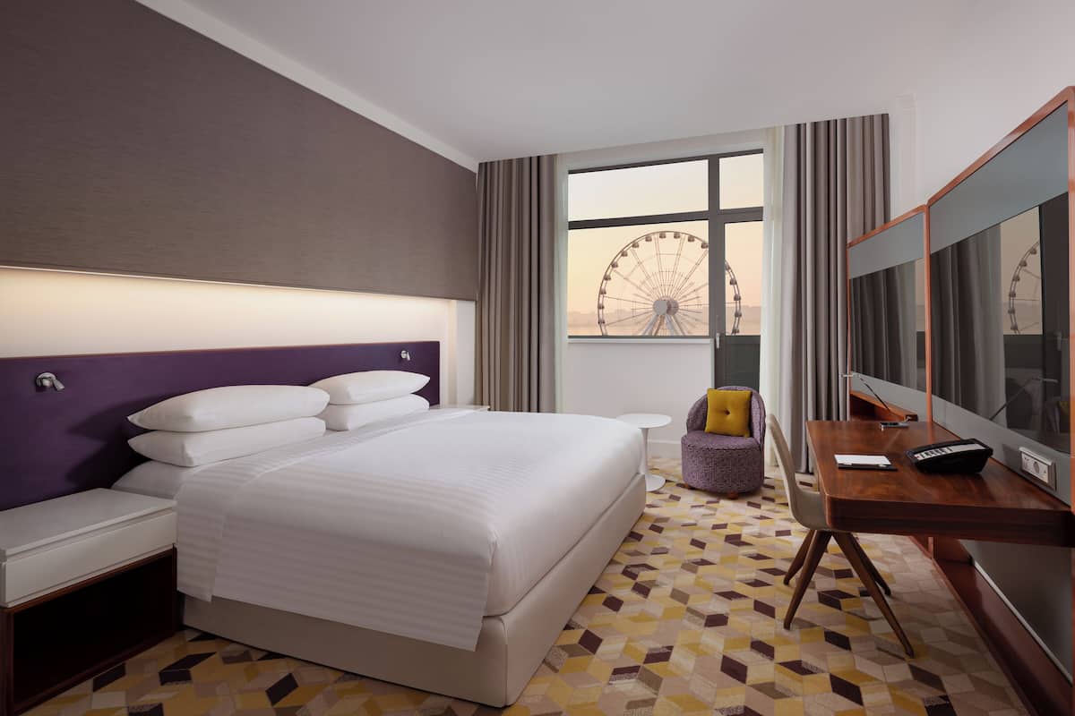 A hotel room with a large bed, a desk with a computer, a chair, and a view of a Ferris wheel.