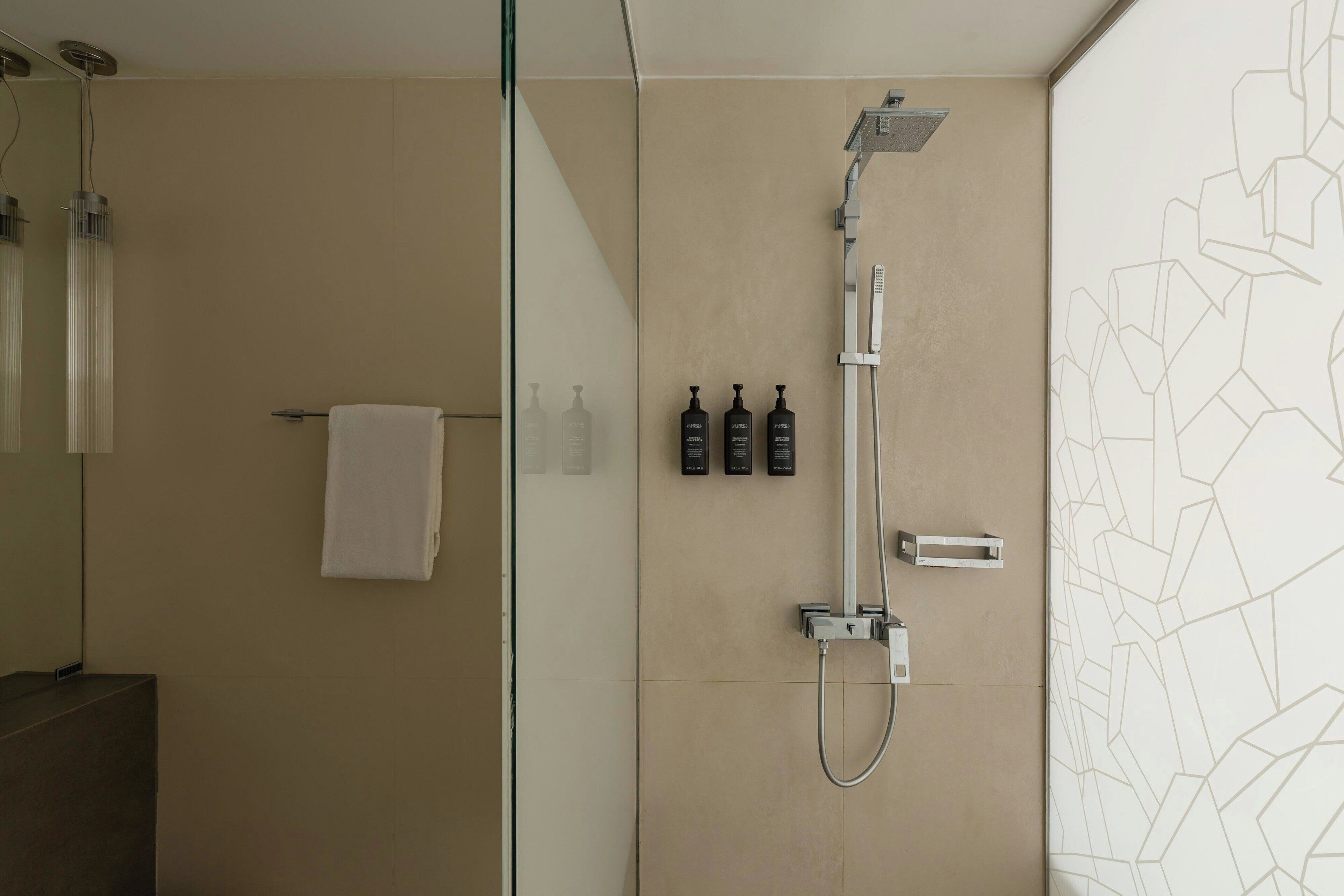 Een moderne badkamer met een douchecabine van glas, een handdoekrek en drie flesjes toiletartikelen aan de muur.