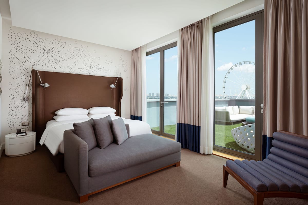 A modern hotel room with a large bed, a sofa, a small table, and a view of a Ferris wheel.