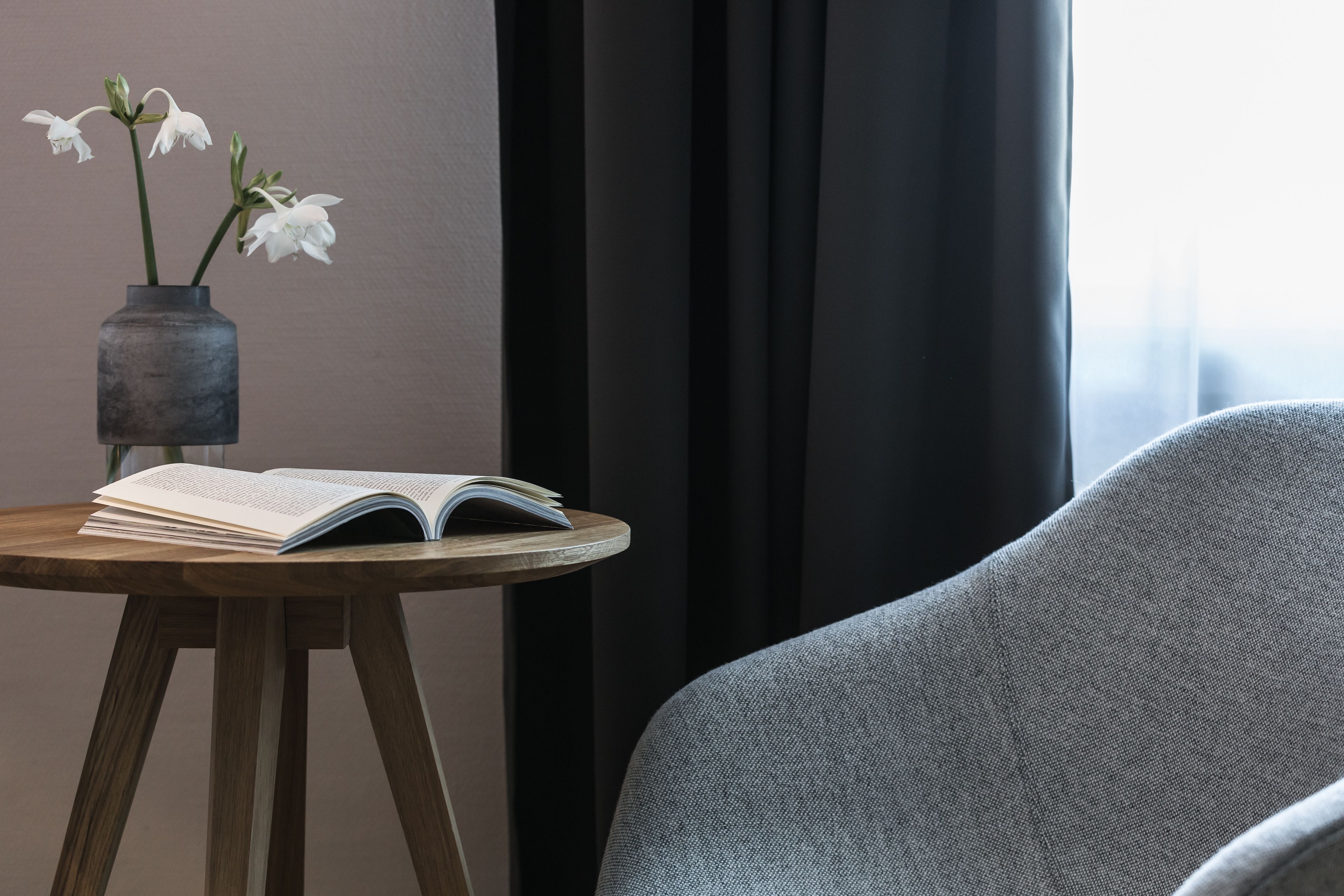 A room with a round wooden table, a book, and a vase with white flowers.
