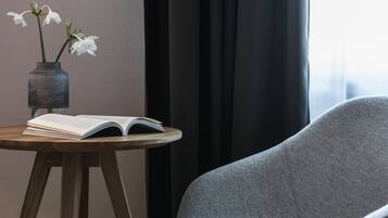 A room with a round wooden table, a book, and a vase with white flowers.