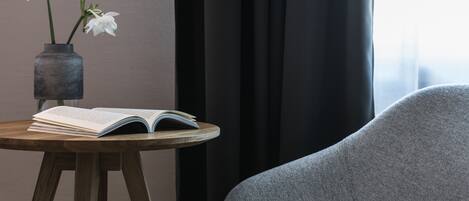 Um quarto com uma mesa redonda de madeira, um livro e um vaso com flores brancas.