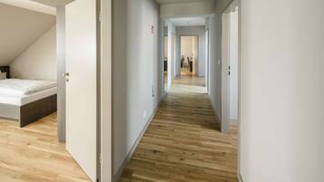 Ein moderner Hotelkorridor mit Holzboden, weißen Wänden und einem sichtbaren Schlafzimmer mit Bett und Schreibtisch.