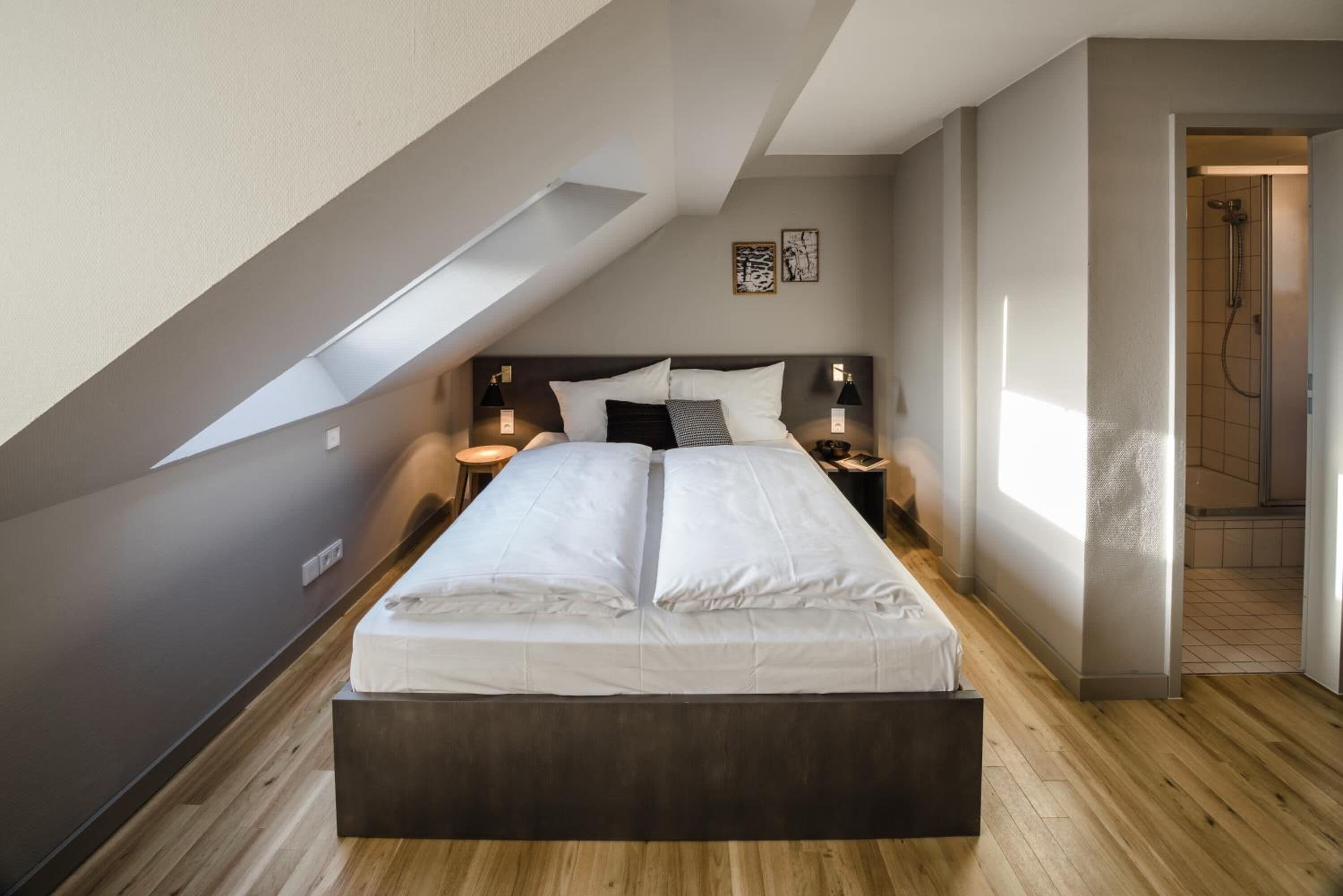 A modern bedroom with a large bed, wooden flooring, and a skylight.