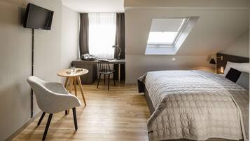 Habitación de hotel moderna con cama, escritorio con silla, televisor montado en la pared y tragaluz.