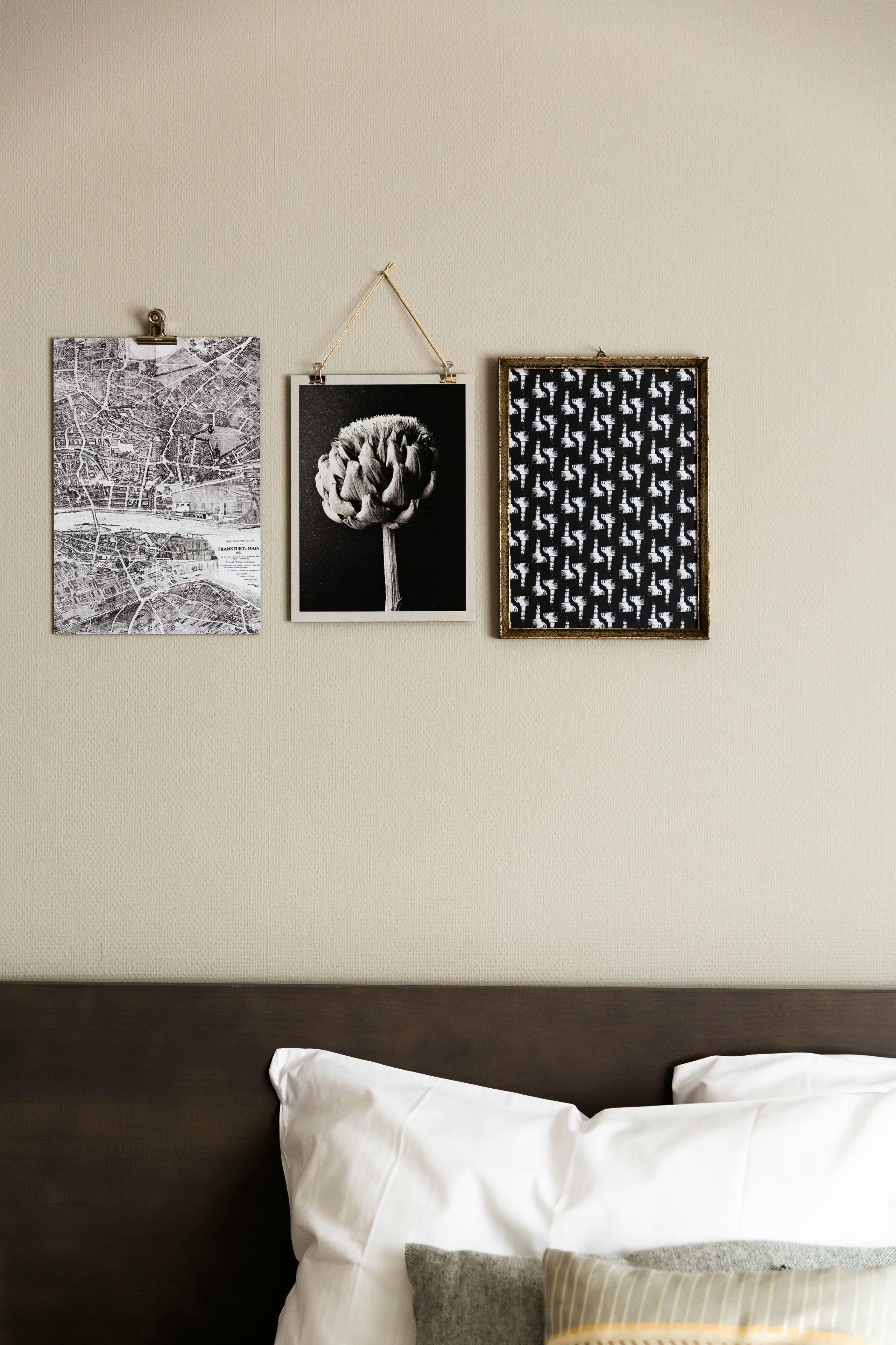 Drie ingelijste foto's aan een muur boven een bed met witte en grijze kussens.