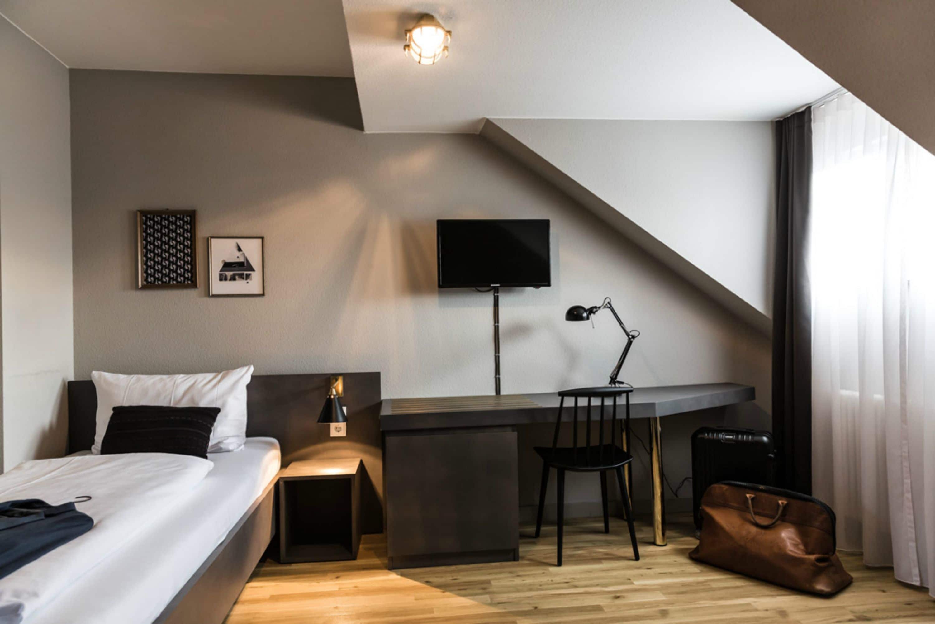 Una habitación de hotel moderna con cama, escritorio, silla y televisor.