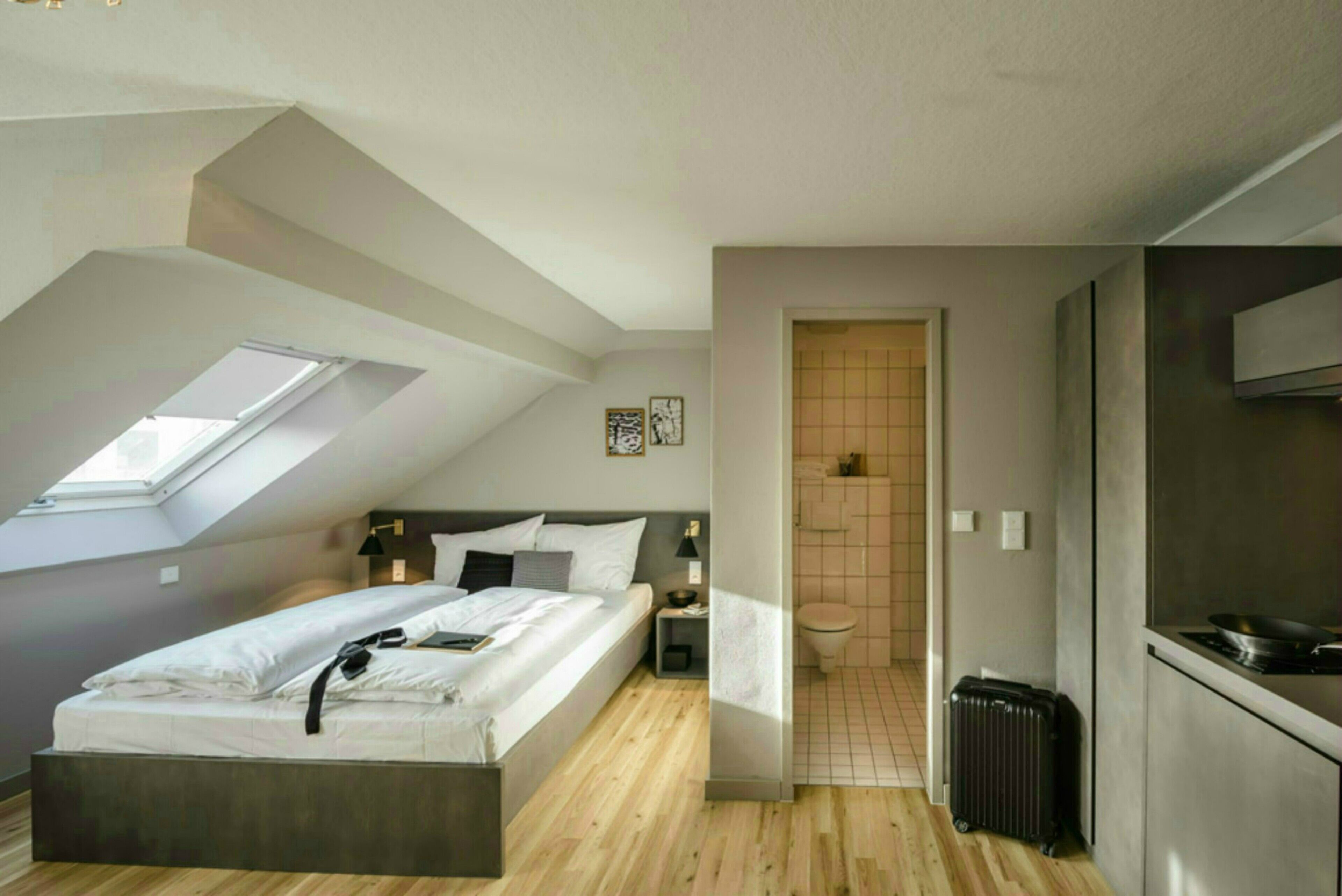 Een moderne slaapkamer met dakraam, een bed, een nachtkastje en uitzicht op een badkamer.