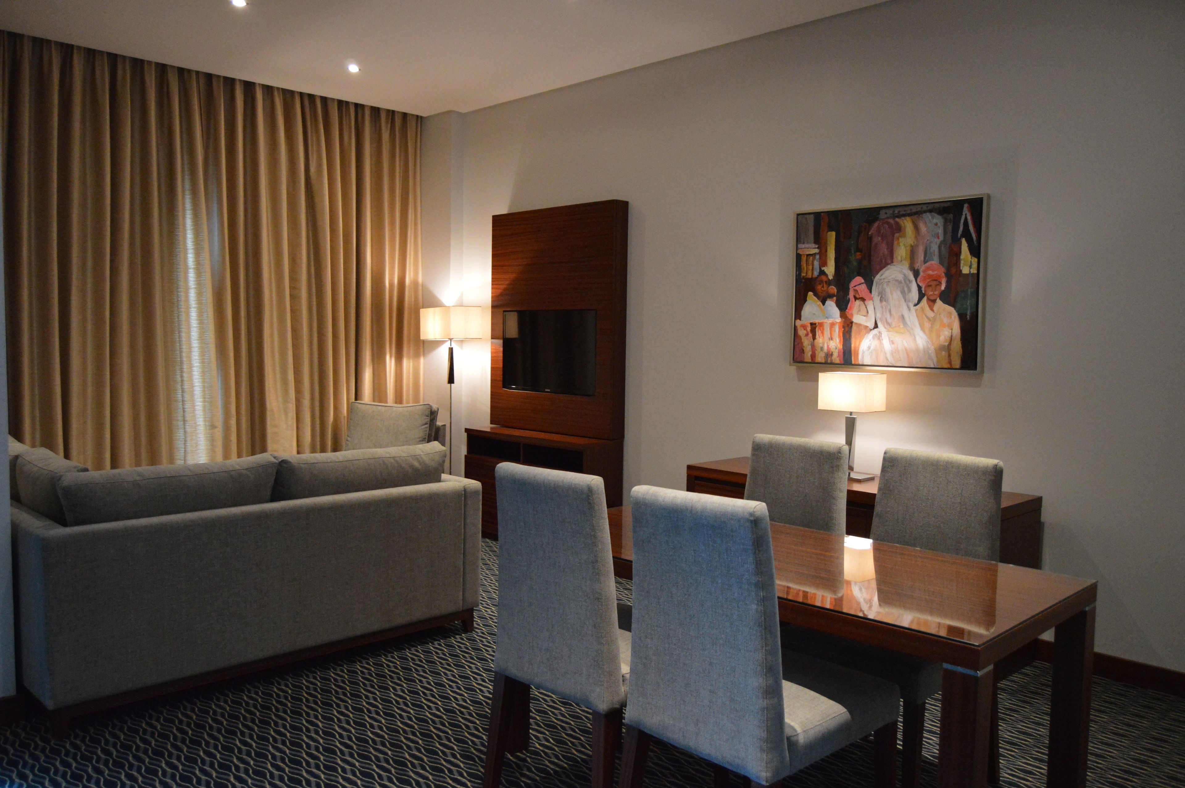 A hotel room with a sofa, two armchairs, a wooden dining table, and two lamps.