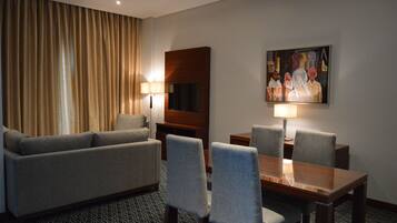 Habitación de hotel con sofá, dos sillones, una mesa de comedor de madera y dos lámparas.