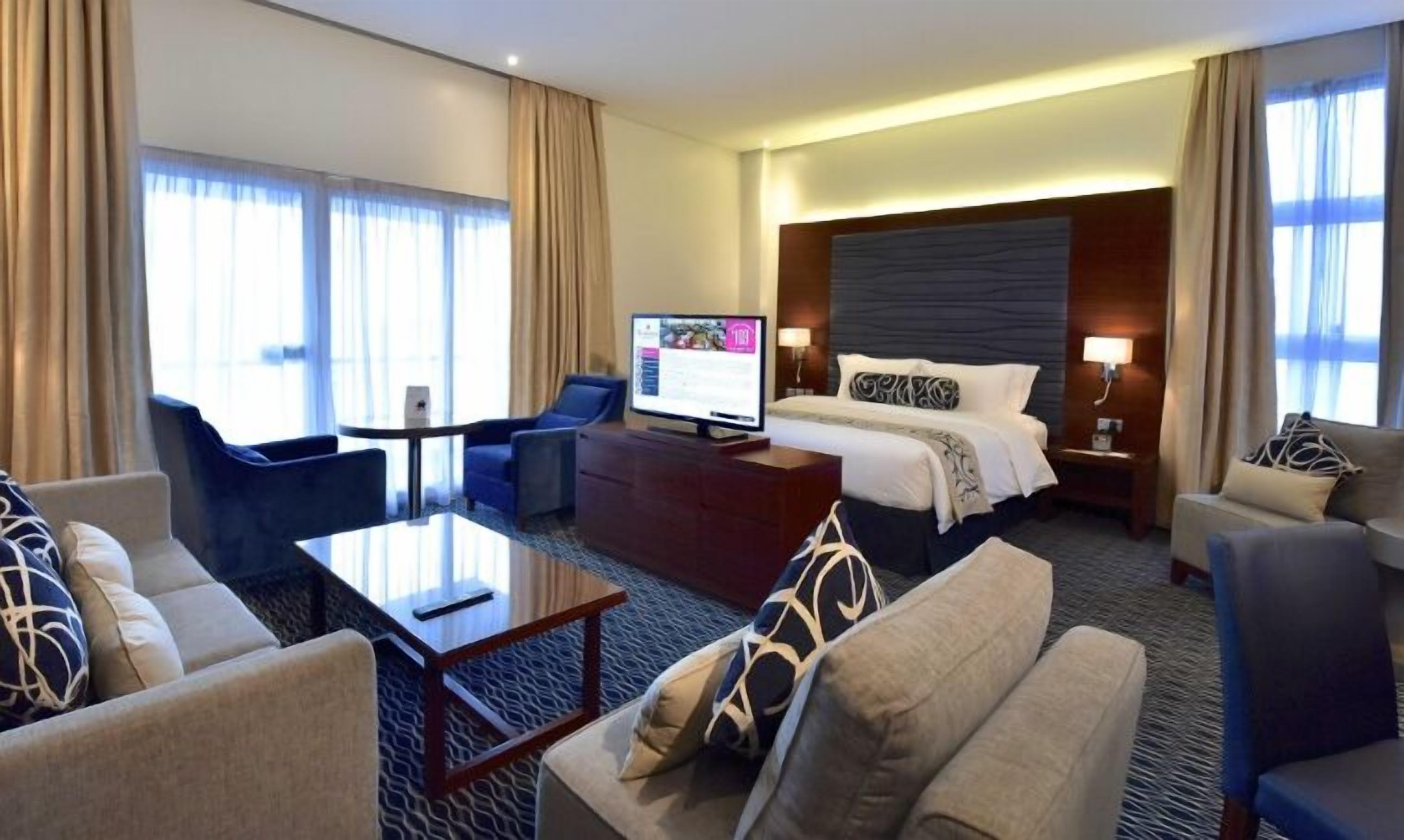 A hotel room with a bed, a desk, a chair, a sofa, and a TV.