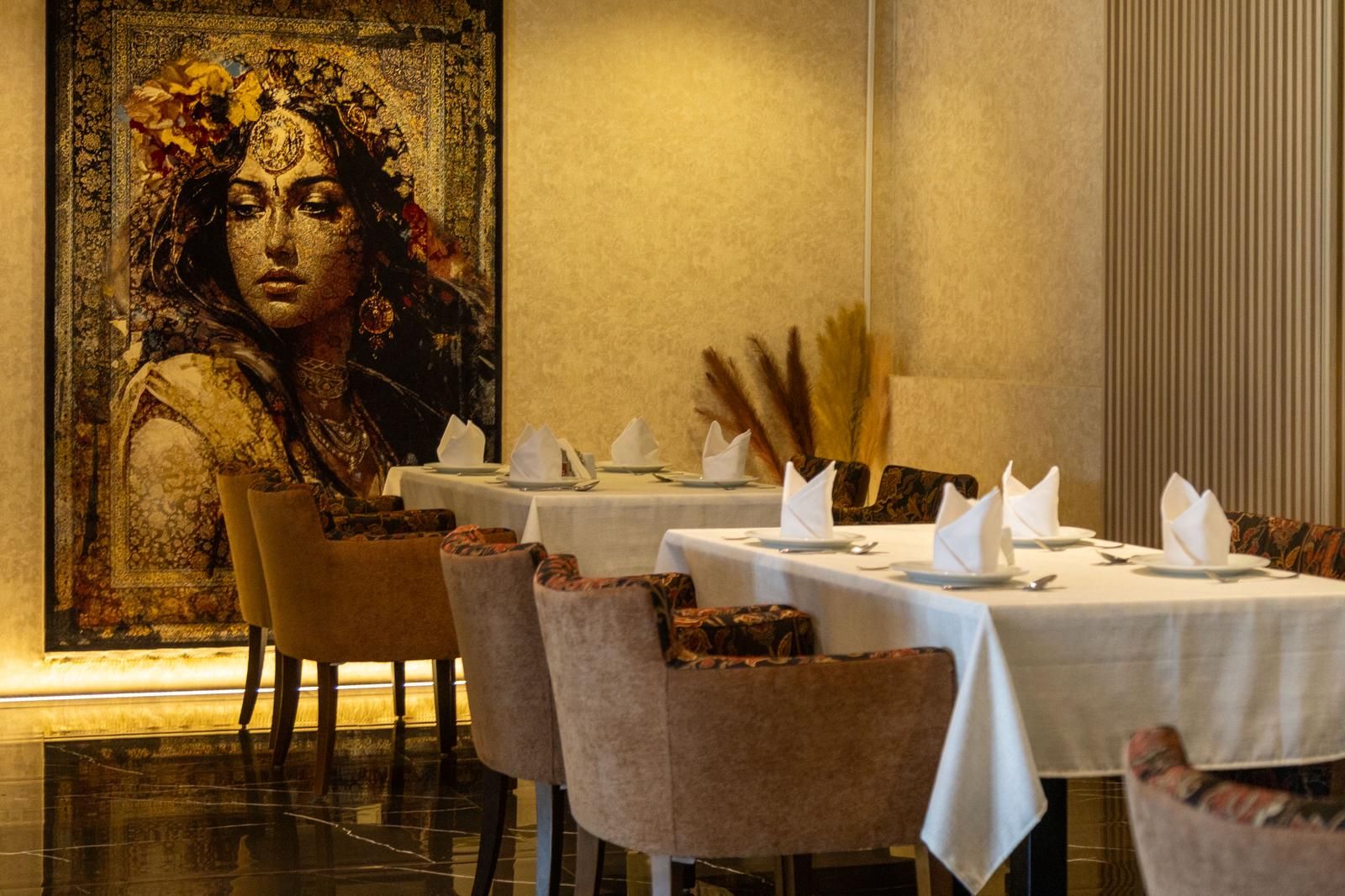 Un comedor con mesas dispuestas para el servicio, sillas y un cuadro decorativo grande en la pared.