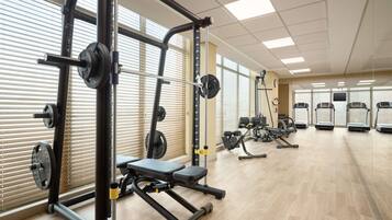 Un gimnasio con diverso equipo de ejercicio, incluyendo una estructura para sentadillas, bancos y cintas de correr.