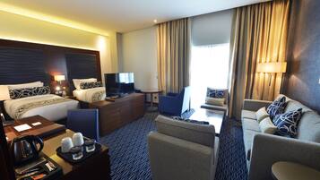 Une chambre d’hôtel équipée d’un lit, d’un bureau avec une bouilloire, d’une télévision, d’un canapé et d’une chaise.