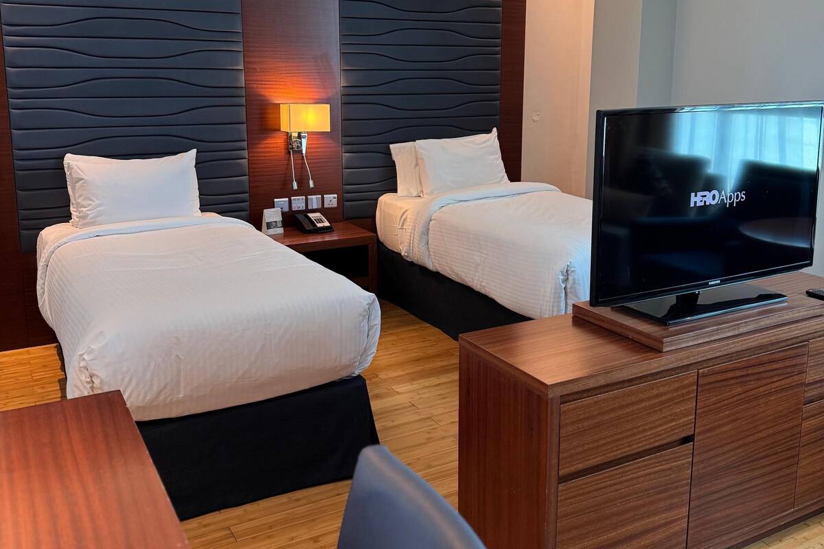 Une chambre d’hôtel avec deux lits, une télévision, un bureau en bois et une lampe.