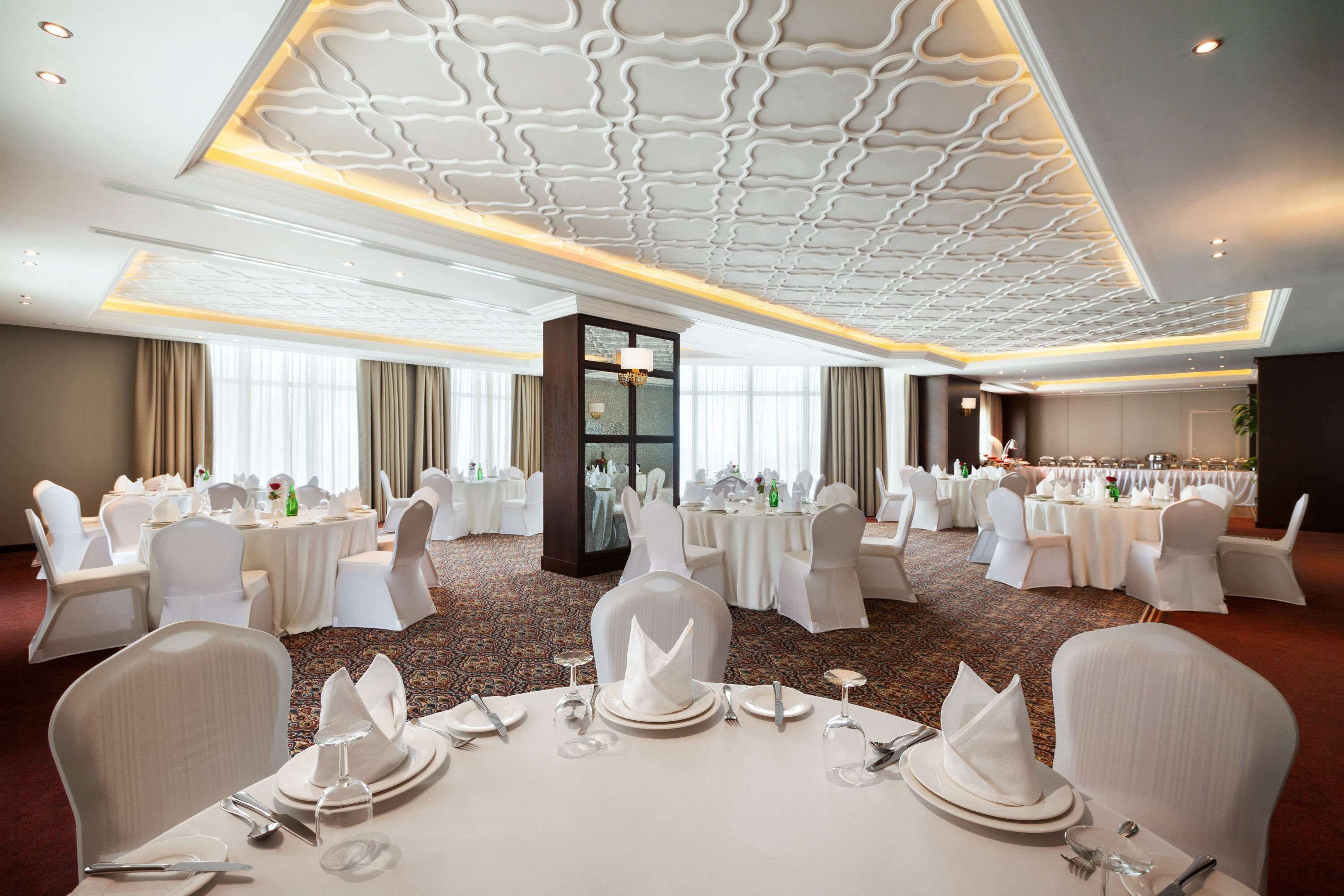 A banquet hall with round tables set for dining, white chairs, and a decorative ceiling.