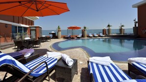 Zona junto a la piscina con sillones de descanso, sombrillas y vista al océano.