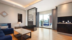Un salon moderne avec un canapé, une table basse et un téléviseur. Il y a un coin cuisine avec des placards et une table à manger. La pièce est dotée d'une grande fenêtre offrant une vue sur la ville.