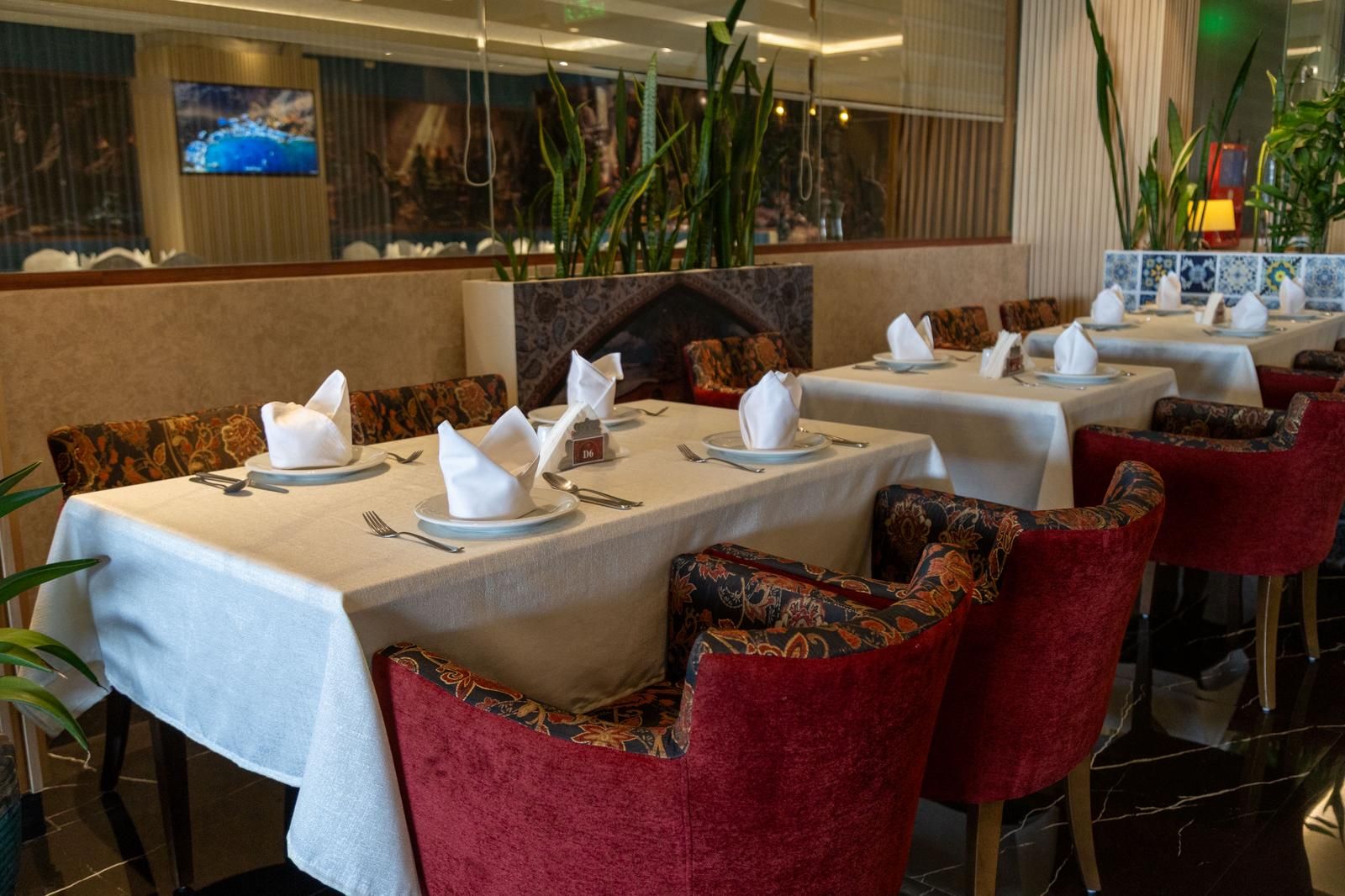 Un restaurante con mesas dispuestas para comer, con sillas tapizadas en rojo y un salpicadero de azulejos.