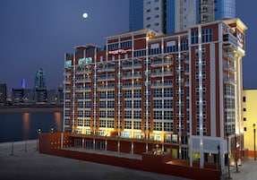Un hotel de varios pisos con balcones, una zona de piscina y vistas del horizonte de la ciudad.