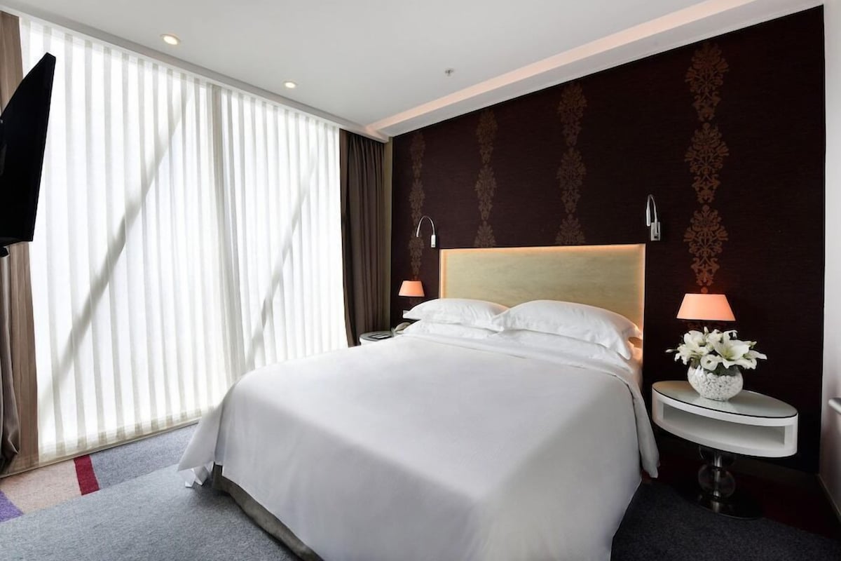Hotelkamer met een groot bed, een televisie, nachtkastje met lamp en raam met gordijnen.