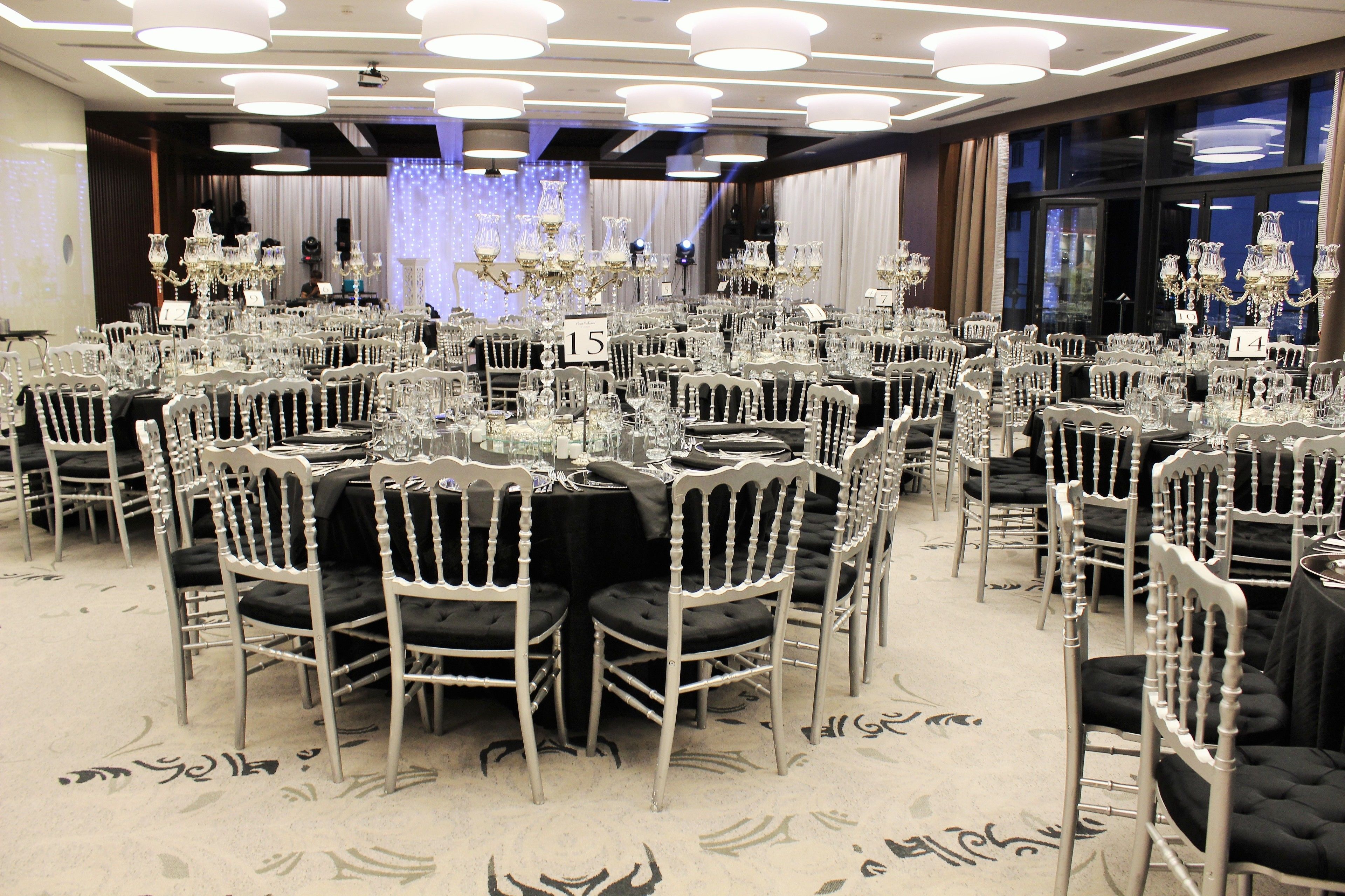 Un salón de banquetes con mesas redondas, sillas blancas y candelabros.
