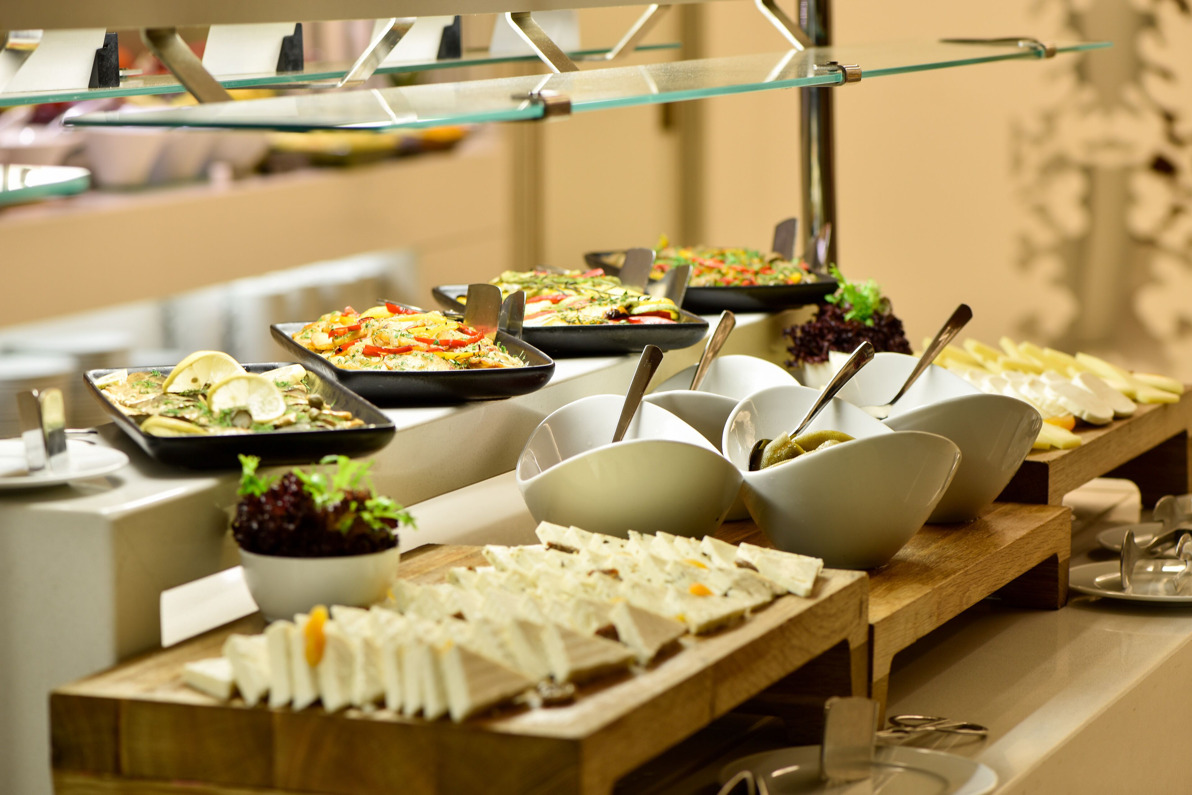En buffet med forskellige retter, herunder salater, kød og oste, anrettet på et langt bord med serveringsbestik.
