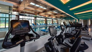 Ein Fitnessstudio mit Trainingsgeräten und einem durch Glaswände einsehbaren Poolbereich.