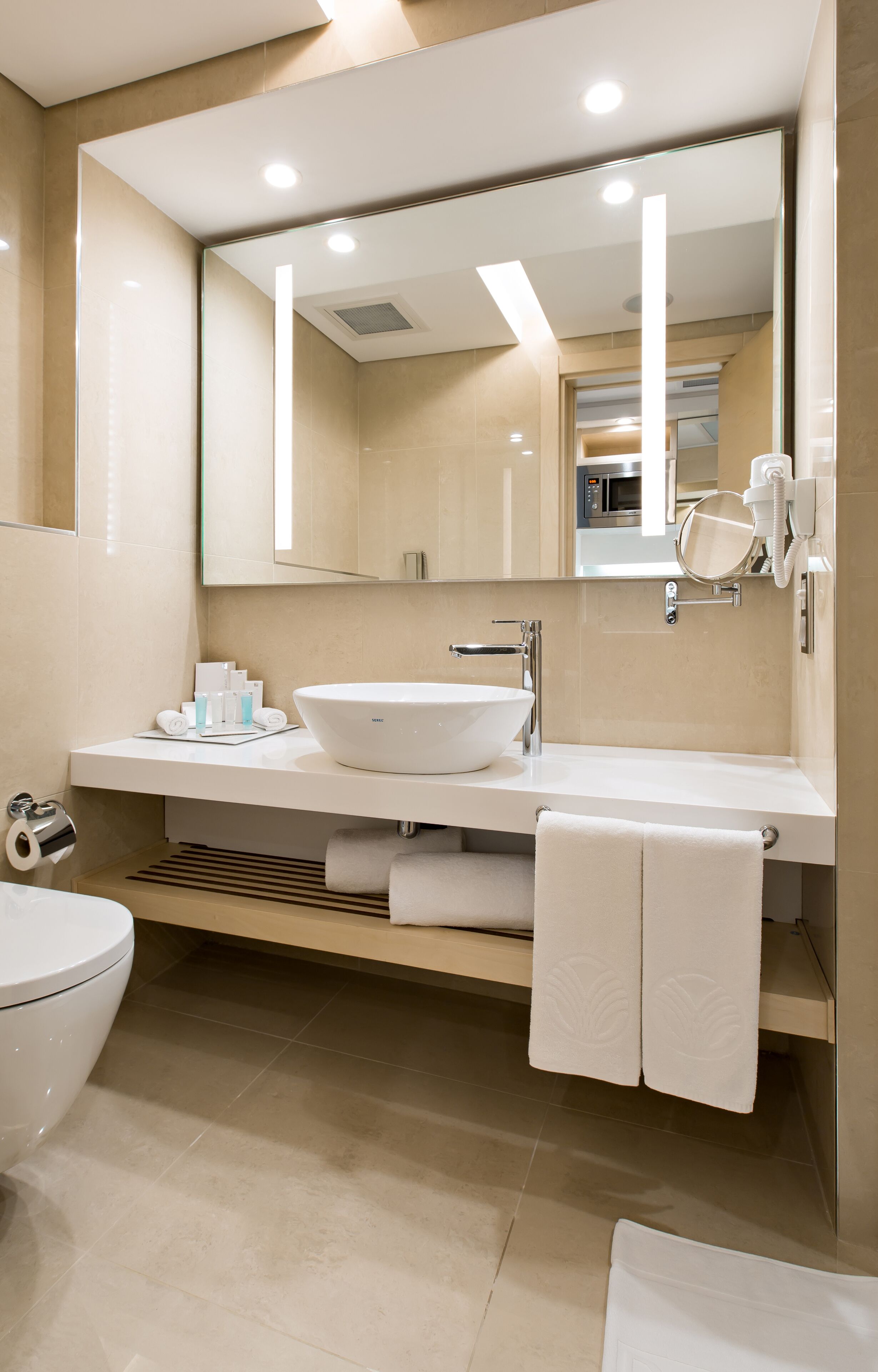 A modern bathroom with a large mirror, a white sink, and a toilet.