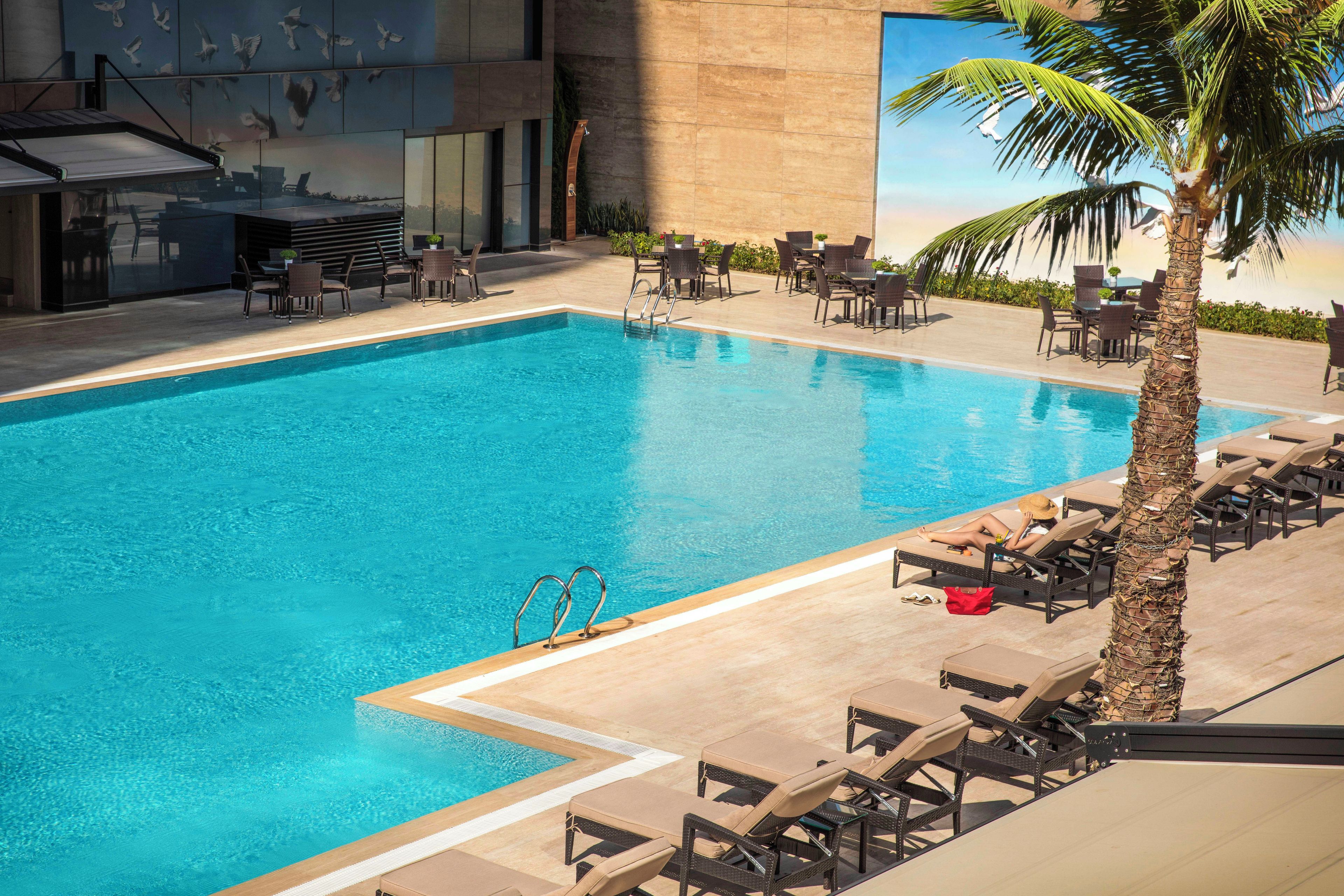 Un área de piscina con sillones de descanso, una palmera y una zona de comedor con mesas y sillas.