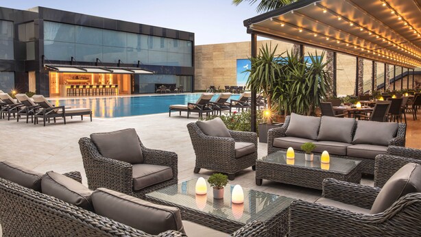 A modern outdoor lounge area with wicker furniture, a pool, and a bar. - Tango Arjaan by Rotana Istanbul (Istanbul)