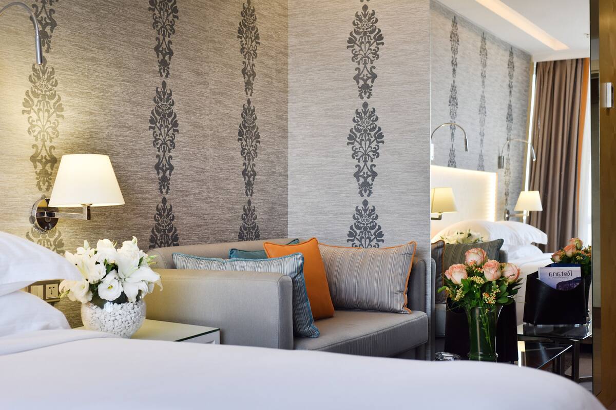 A hotel room with a sofa, a vase of flowers, a lamp, and a mirror.