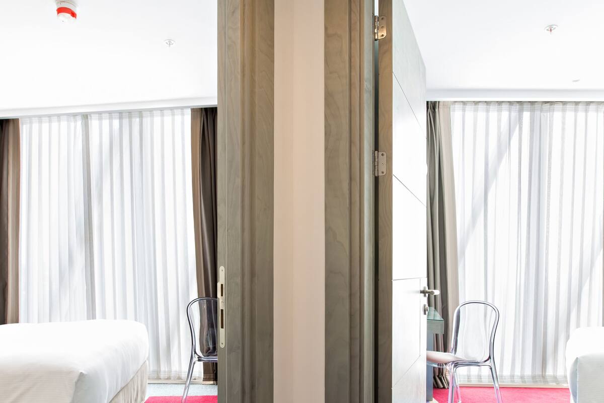 A hotel room with a bed, a chair, and a desk. There is a door leading to another room.